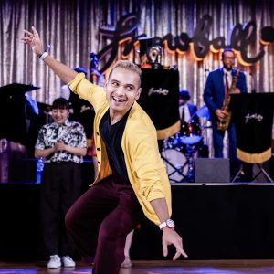 photo of young male swing dancer Farooq Khan in a yellow shirt in front of a live jazz band on stage at a swing dance event